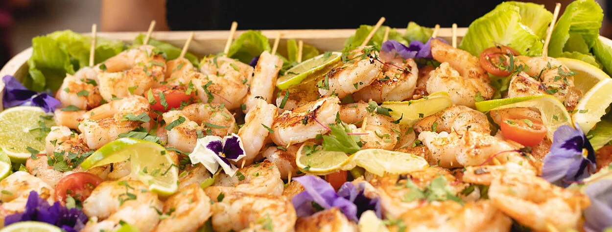 A platter full of qld prawn skewers topped with lemon and micro flowers ready for guests at a wedding to enjoy