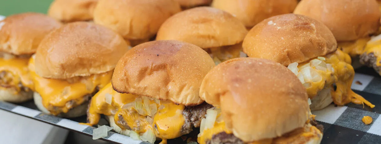 A close up of Cheeseburger sliders. the Cheese is melting and dripping onto the platter.  