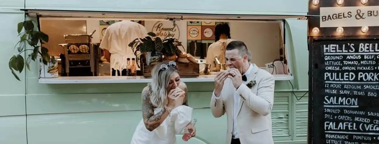 Bride and groom standing in front of our food truck eating bagels for their wedding meal.