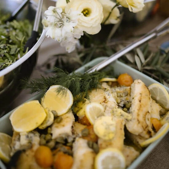 Dishes of food spread out on a buffet table, styled with flowers, lemons and olive branches